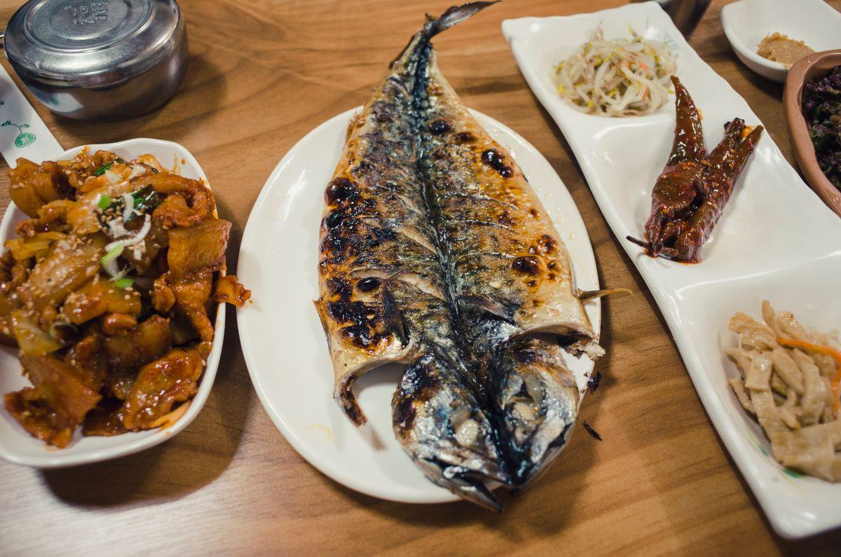Traditional Korean seafood dinner with grilled fish, seasoned side dishes, and rice served on a wooden table