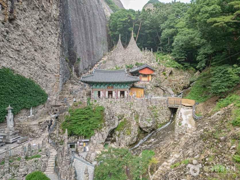 Tapsa Temple complex with dozens of stone pagodas of varying heights nestled against the sheer cliff face of Maisan, with a traditional Korean temple pavilion visible