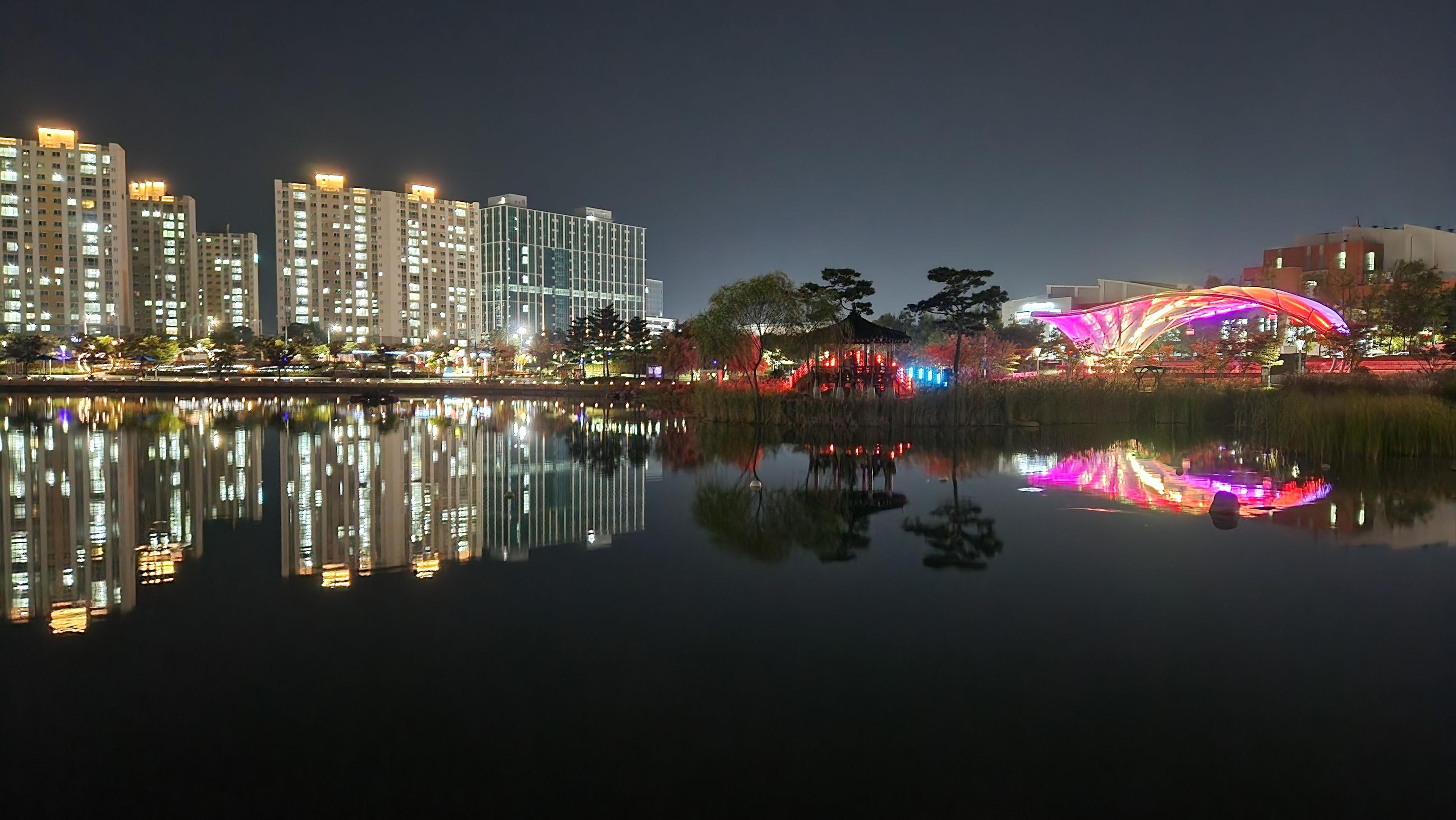 Illuminated buildings and their colorful reflections in a calm Korean lakeside park at night