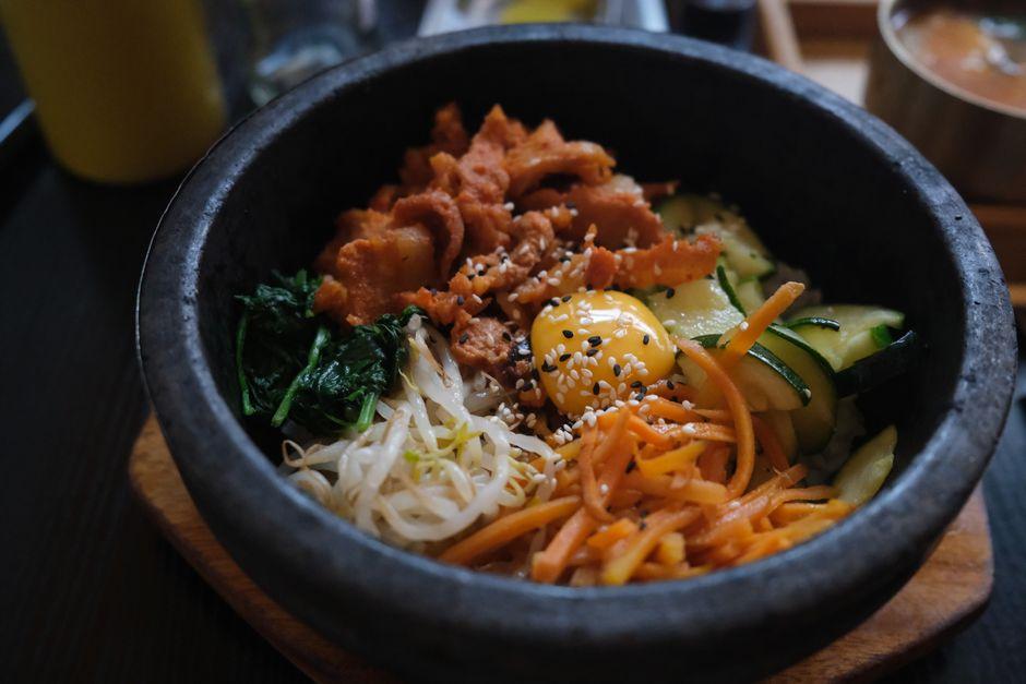 Traditional Korean bibimbap in a bowl with fresh vegetables, beef, and egg yolk