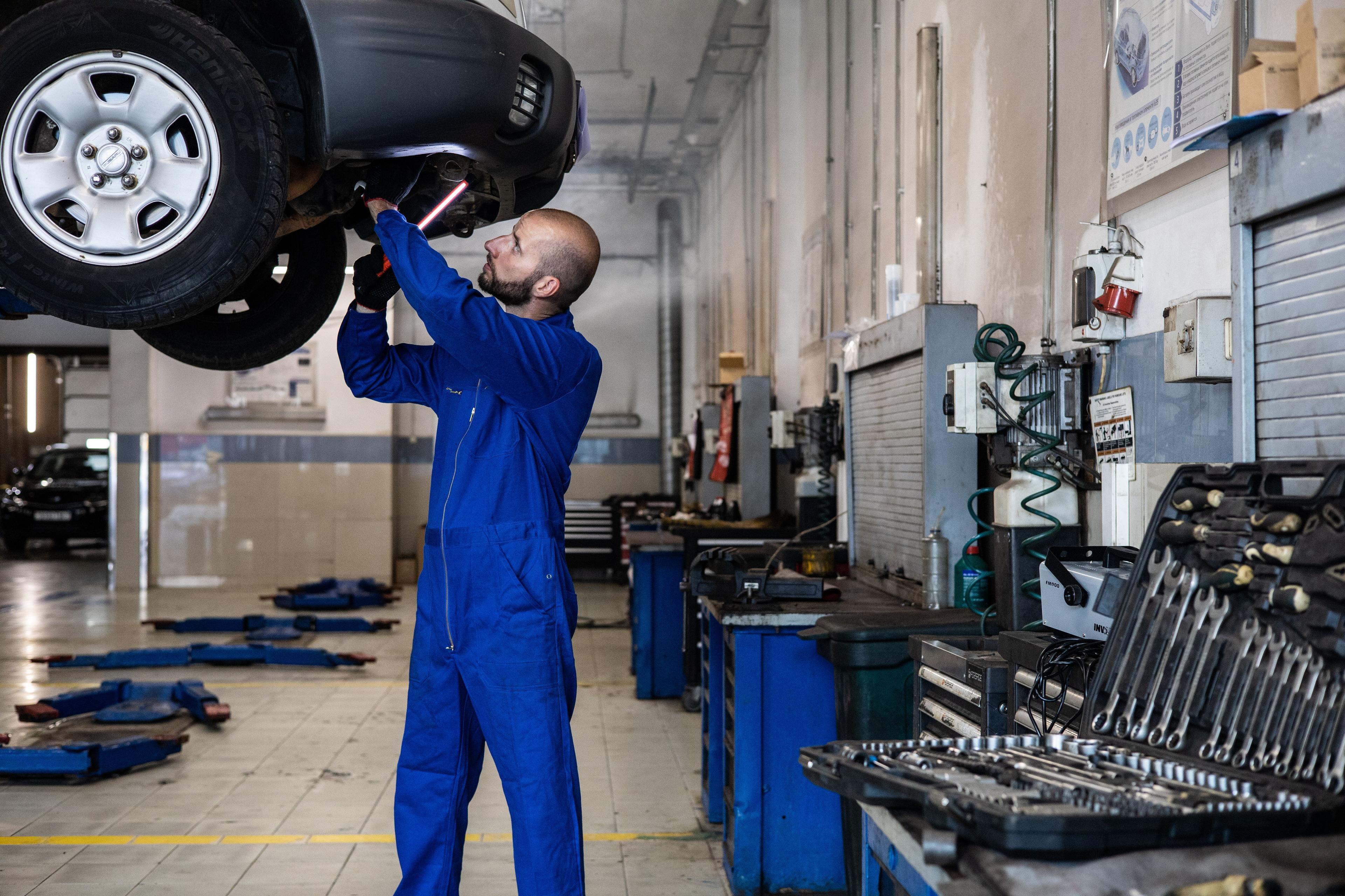 Mechanic inspecting a raised rental car for damage during a Korea car return assessment