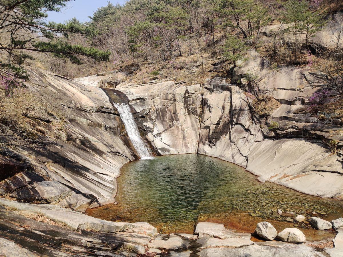 Natural waterfall cascading into a clear rock pool surrounded by lush green forest in Miryang, South Gyeongsang Province