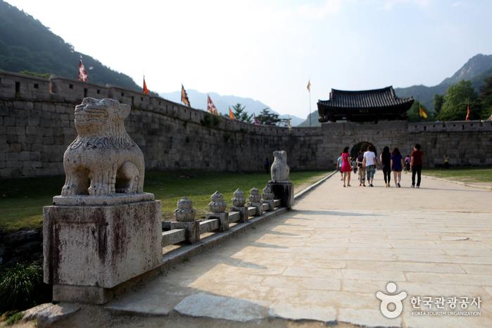 Hikers walking along the shaded forest trail of Mungyeong Saejae pass between the historic fortress gates