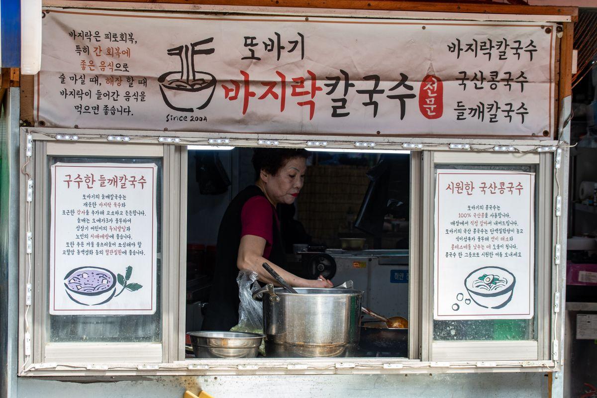 Korean noodle vendor at a traditional Seoul market stall preparing noodles for customers