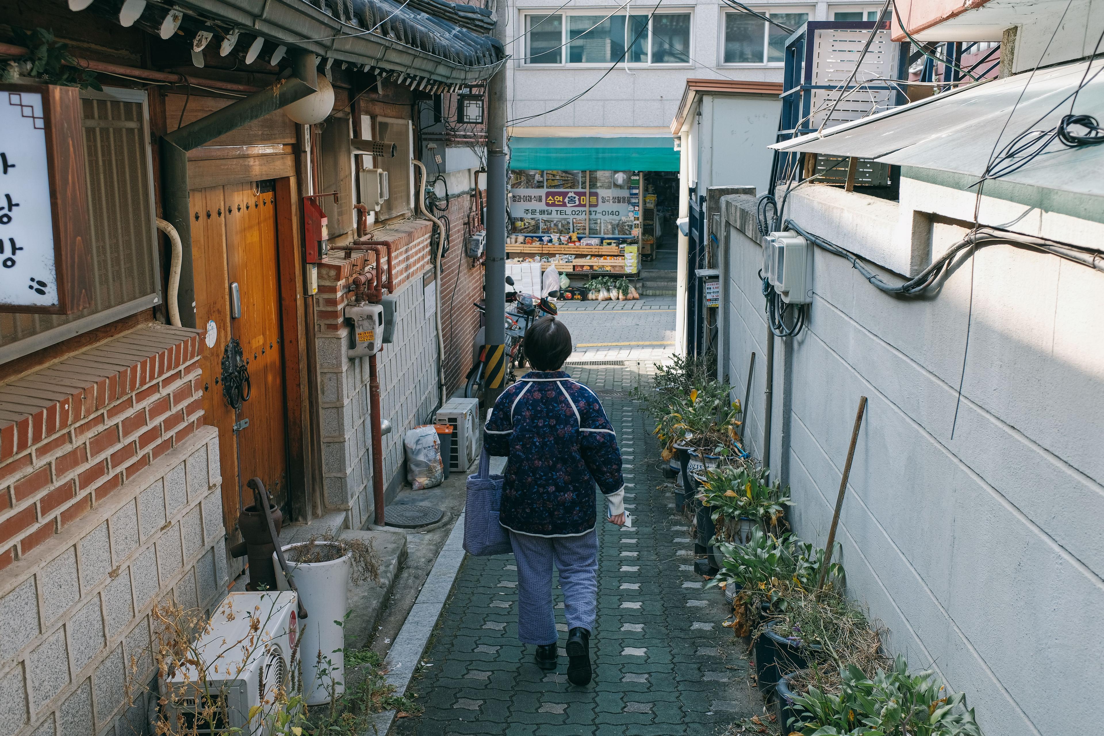 Woman walking down a narrow traditional alley in Seoul lined with traditional Korean buildings
