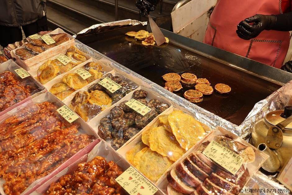 Sliced squid sausage (ojingeo sundae) and other refugee-style street food displayed at an Abai Village food stall